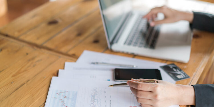 Business woman hand with Financial charts and laptop on the tabl Alianza entre ADP y Convera