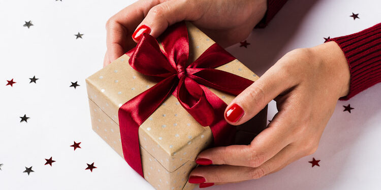 Woman hands holding christmas holiday gift box on decorated festive table Devoluciones navideñas
