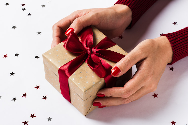 Woman hands holding christmas holiday gift box on decorated festive table Devoluciones navideñas