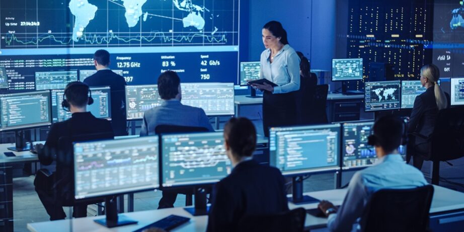 Female Project Leader with Tablet Computer Asks Male Data Science Engineer and Checks Up on His Work Progress. Telecommunications Control Monitoring Room with a Global Map on Big Screen.